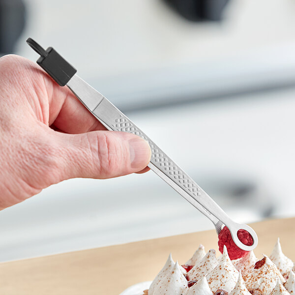 A hand using Mercer Culinary Precision Plus plating tongs to place white cream on a dessert.