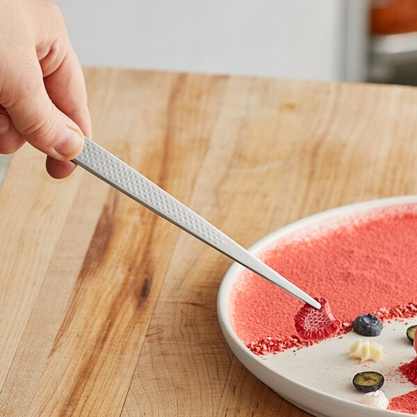 A hand using Mercer Culinary straight plating tongs to plate food.