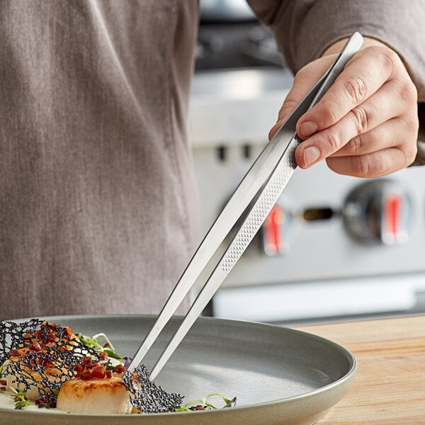 A person using Mercer Culinary plating tongs to plate food.