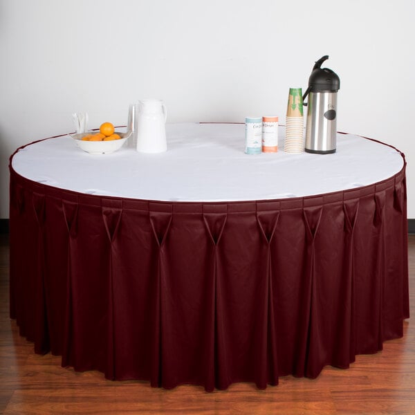 A table with a burgundy Snap Drape Wyndham table skirt on it.
