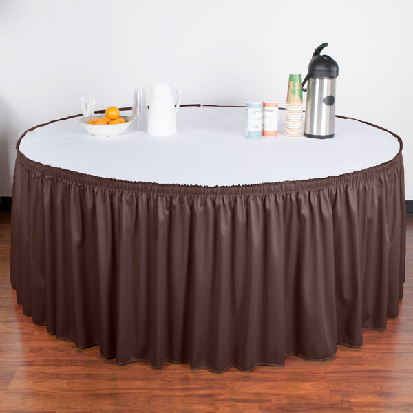 A table with a brown Snap Drape table skirt on it and a bowl of oranges.