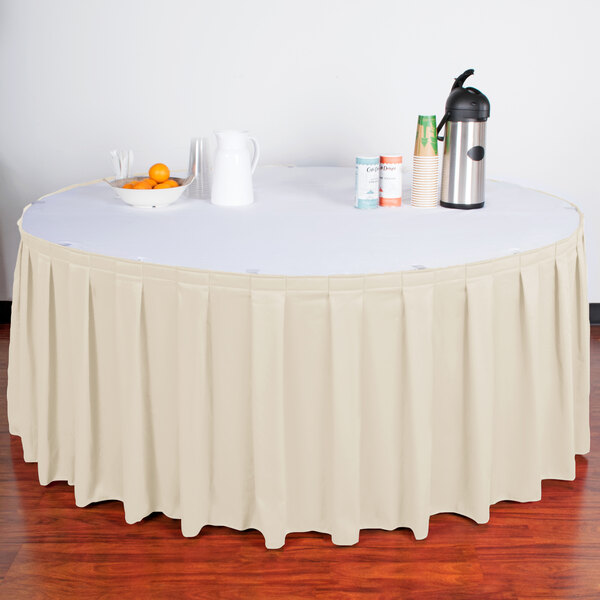 A table with a Snap Drape Bone Box Pleat Table Skirt on it with a black stripe.