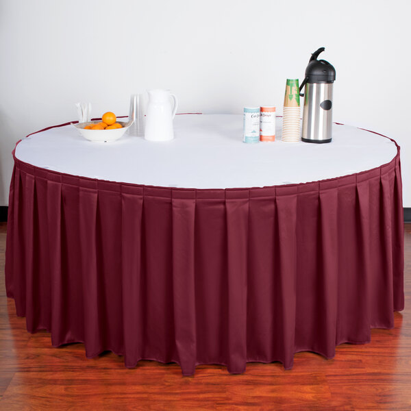 A table with a burgundy Snap Drape table skirt on it and a bowl of fruit.