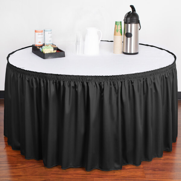 A black Snap Drape shirred pleat table skirt on a table with a black and white tablecloth.