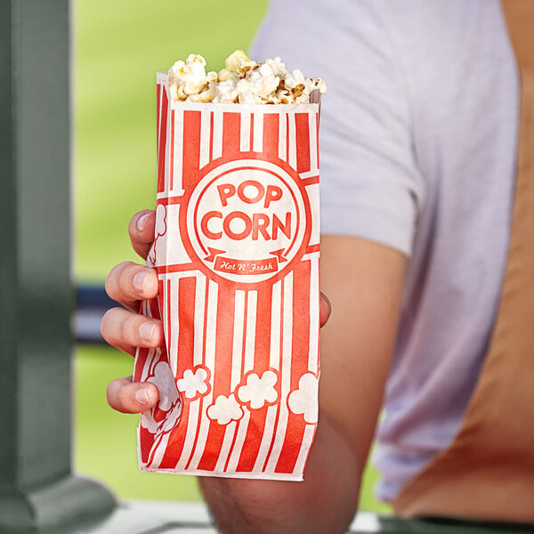 A hand holding a red and white Carnival King bag of popcorn.