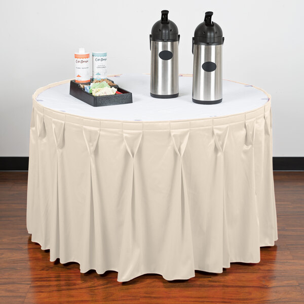 A table with a Snap Drape cream table skirt on it with two containers on it.