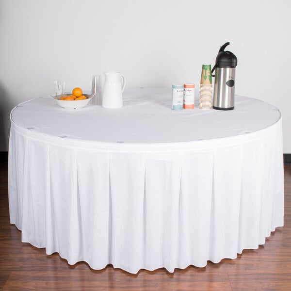 A white table skirt on a table with a white tablecloth and a pitcher of drinks.