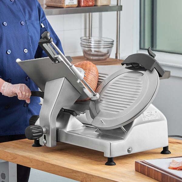 A man using the Hobart EDGE-13 meat slicer to cut ham.