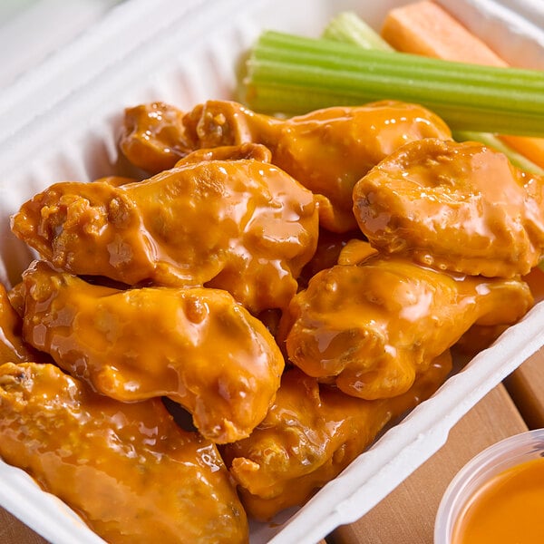 A tray of Louisiana buffalo wings with celery sticks in orange liquid.