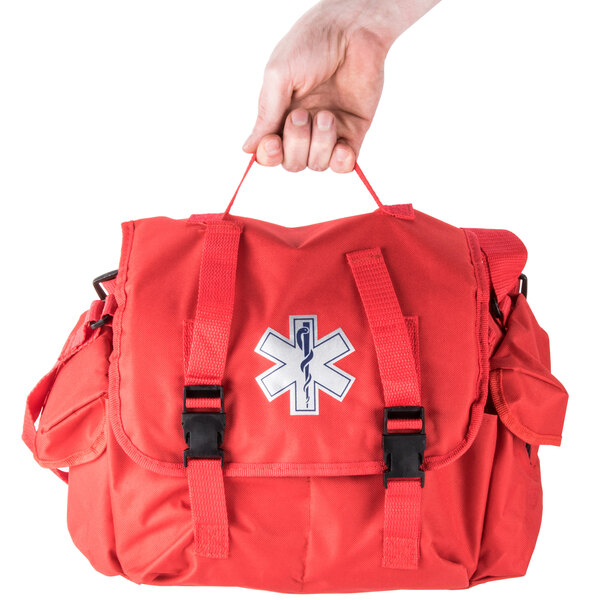 A hand holding a red Medi-First emergency kit with a black cross on it.
