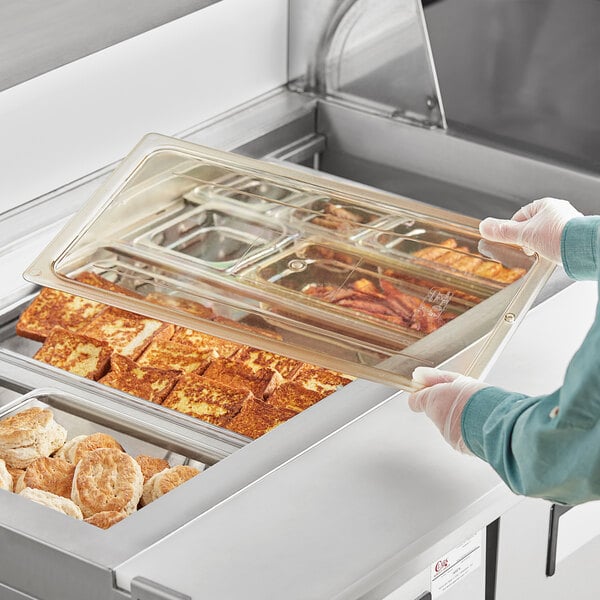 A person putting a Cambro H-Pan lid on a tray of food.