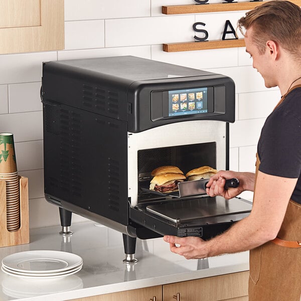 A man cooking sandwiches in a TurboChef Sota rapid cook oven on a countertop.