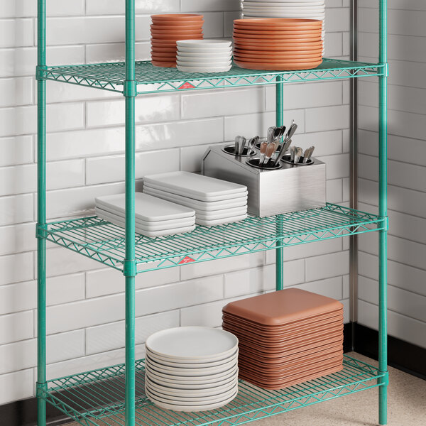 A green wire shelving unit with multiple shelves holding stacks of plates, trays, and a utensil holder.