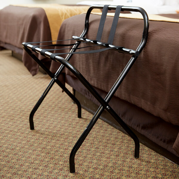 A black metal high back luggage rack with back webbing leaning against a bed.