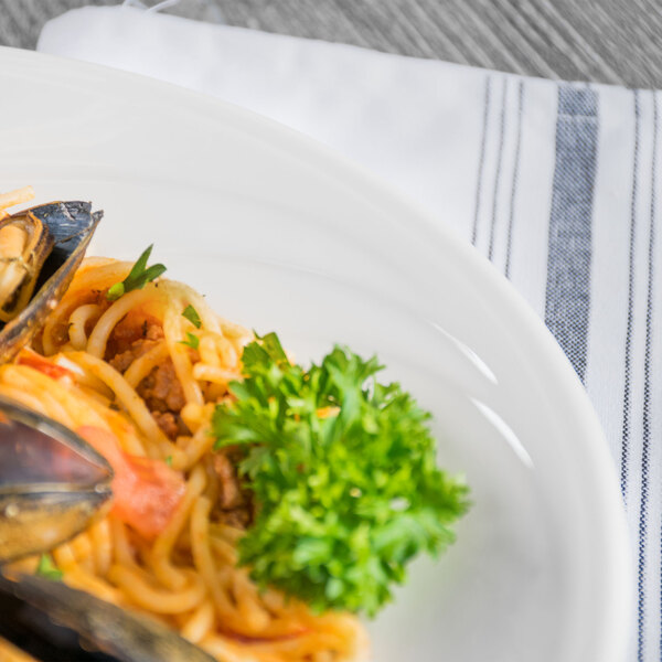 A Libbey white porcelain pasta bowl filled with pasta, mussels, and parsley on a table.