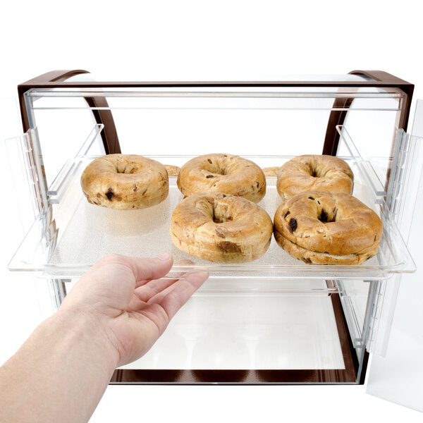 A hand reaching for a tray of bagels in a Cal-Mil iron bakery display case.