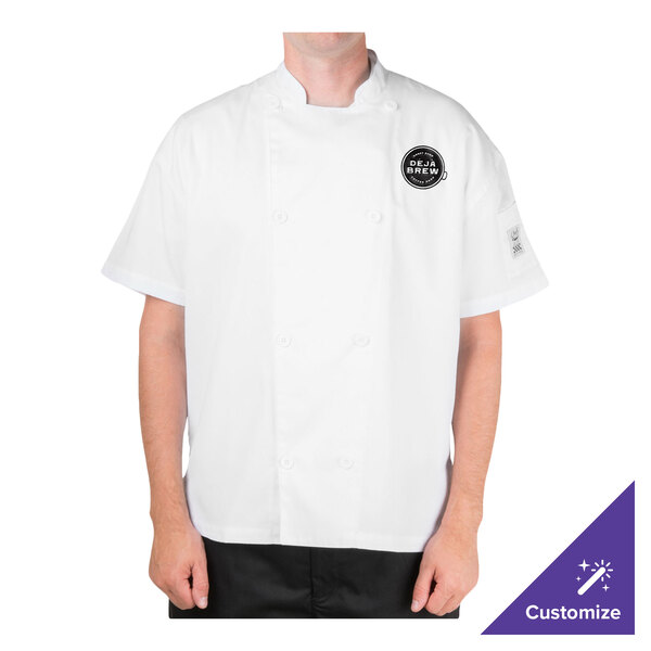A person is wearing a white short-sleeve chef jacket with a black circular logo on the left chest and black pants.