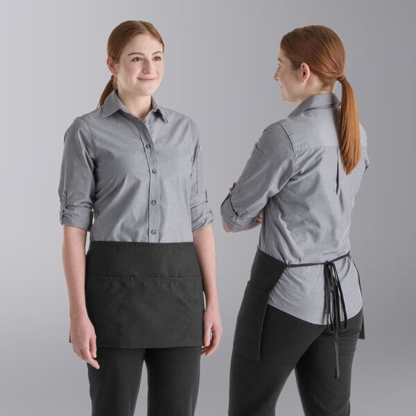 Two women are shown wearing gray button-up shirts and black waist aprons with three front pockets, viewed from the front and back.