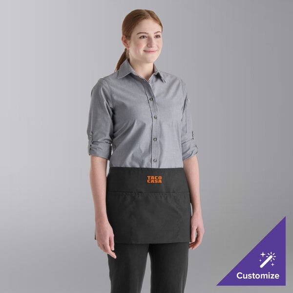 A person is wearing a black waist apron with three pockets and the text 'TACO CASA' embroidered on the front.