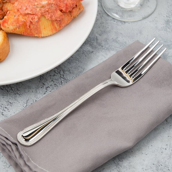 A Bon Chef stainless steel dinner fork on a napkin next to a plate of food.