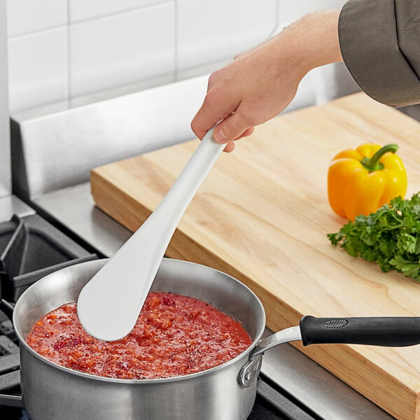 A Mercer Culinary white spootensil stirring red sauce in a pot.