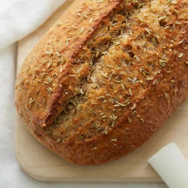 A loaf of bread with seeds on top on a cutting board.