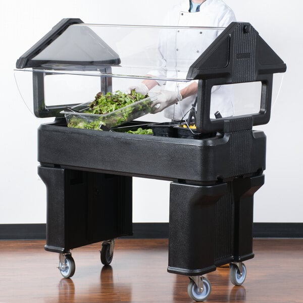 A chef in a white coat and gloves preparing food at a Carlisle Six Star portable salad bar.
