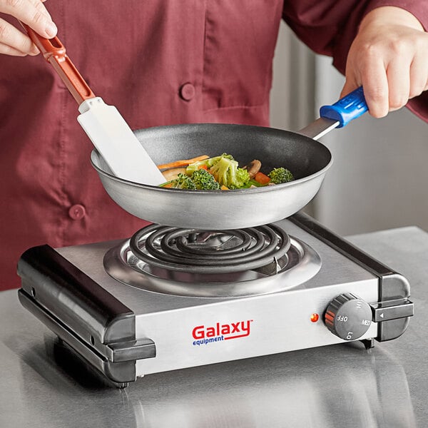 A chef cooking vegetables in a pan on a Galaxy single burner countertop range.