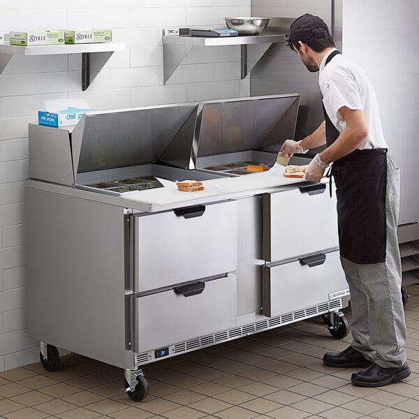 A man in a white shirt and black apron is using a Beverage-Air Elite Series Mega Top Sandwich Prep Table to prepare food.