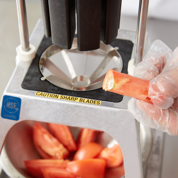 A person using a Vollrath Redco 8 section core replacement blade assembly to core a tomato.