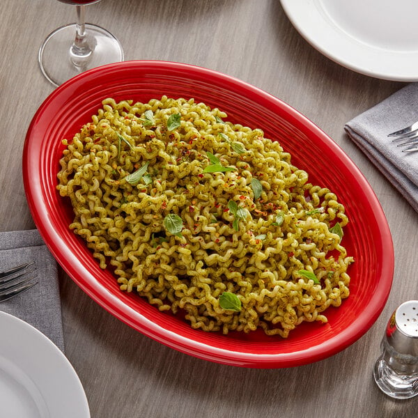 A Tuxton cayenne oval china platter holding pasta with basil on a table with a glass of wine.