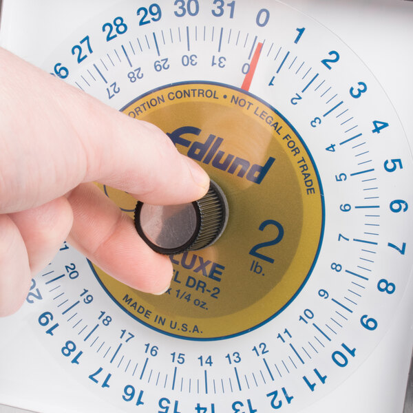 A person using an Edlund Premier Series portion scale with a black plastic knob to adjust the weight.