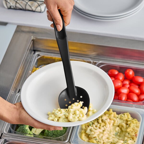 A person using a black Cambro perforated spoon in a bowl of macaroni and cheese on a salad bar counter.