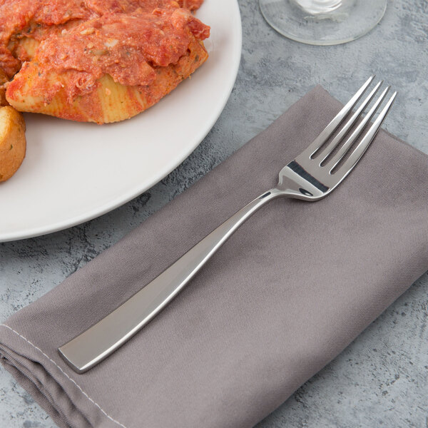 A Bon Chef stainless steel dinner fork on a napkin next to a plate of food.