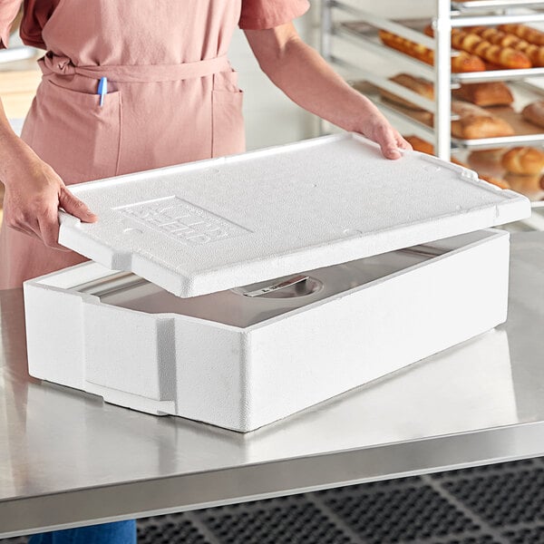 A woman holding a white Lifoam Chef's Caddy foam food pan carrier with a lid open.