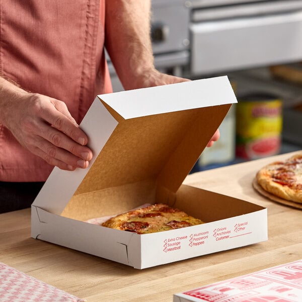 A white, clay-coated pizza box being opened, containing a slice of pizza.