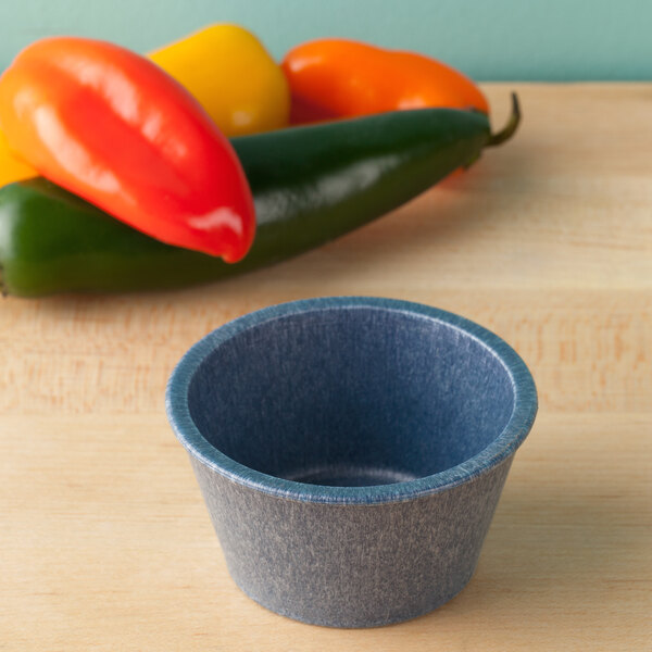 A blue HS Inc. polyethylene ramekin on a table next to a pile of red peppers.