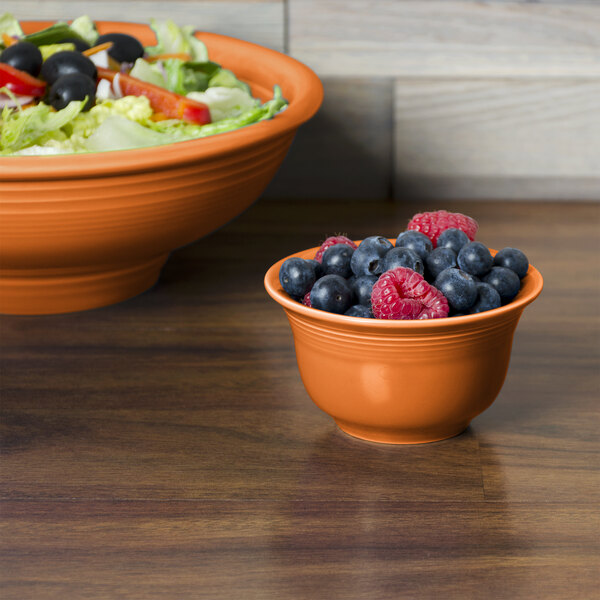 A bowl of salad and a bowl of fruit served in Fiesta Tangerine China Bowls.