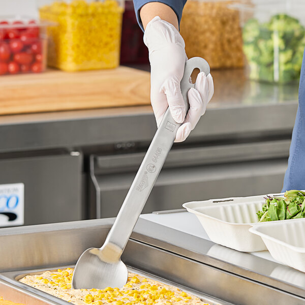 A person in a white apron using a Vollrath stainless spoon to scoop food.