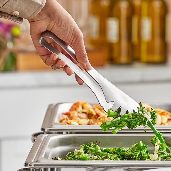 A person holding Carlisle stainless steel serving tongs to a plate of food.