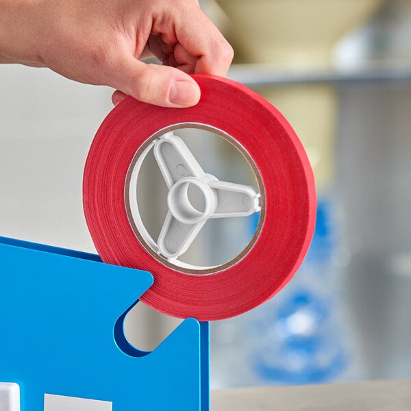 A roll of red poly bag sealer tape being placed into a blue tape dispenser.