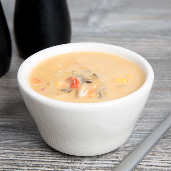 A Tuxton eggshell china bouillon cup filled with soup on a table with a spoon.