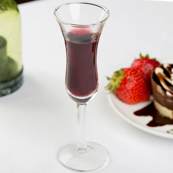 A Libbey tall dutch cordial glass filled with red liquid next to a plate of strawberries.