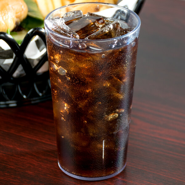 A Cambro clear plastic tumbler filled with brown liquid and ice on a table.