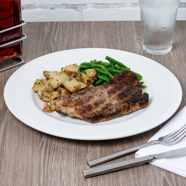 A white porcelain plate with steak and potatoes on a table.