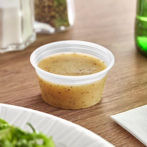 A clear plastic Dart souffle container filled with sauce on a table.