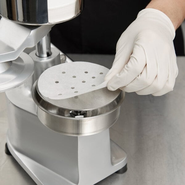 A hand in a white glove using a machine to make a roll of perforated patty paper.