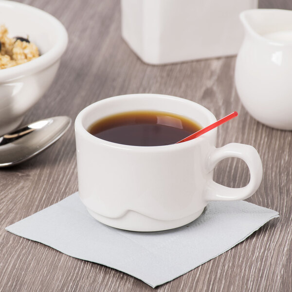 A white Libbey porcelain cup of coffee with a spoon on a saucer.