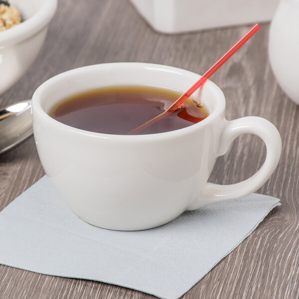 An ivory porcelain coffee cup filled with coffee and a spoon on a table.