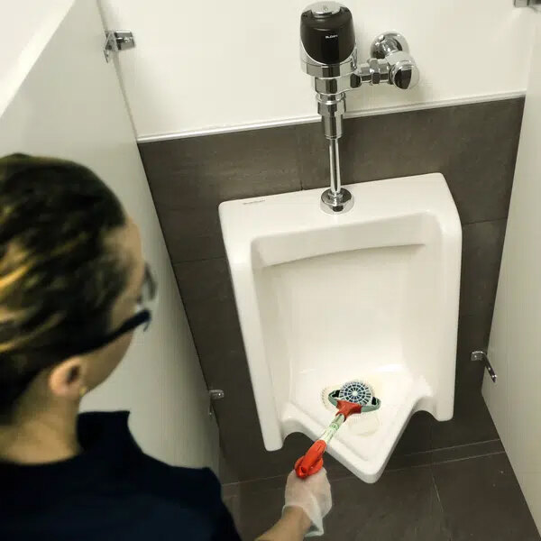 A woman using an Unger NiftyNabber to clean a urinal.